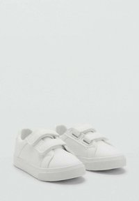 Ett par små vita sneakers med dubbla kardborreband, texturerade gummisulor och slät ovandel på en enfärgad bakgrund.