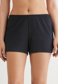 Mörkblå shorts i ett mjukt material, med elastisk midja och dekorativt spetsdetalj på sidan. Minimala sömmar och enkel design.
