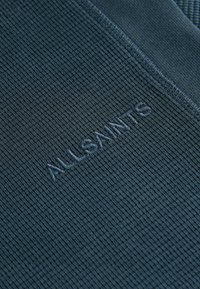 Tamsiai mėlyni smulkūs audiniai su išsiuvinėtu "ALLSAINTS" logotipu. Tekstūra subtili, kraštai lygūs.