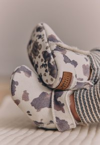 Chaussons blancs et gris avec un motif tacheté en gris et violet, présentant une surface texturée et un accent en cuir marron.