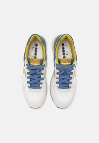 White and blue athletic shoes with yellow accents. Mesh and suede materials, round toes, and flat laces. Diadora logo on the tongue.