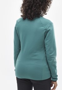 Tiefblaue, langärmelige Bluse mit einer glatten Textur. Verfügt über einen runden Saum und subtile Nähdetails an den Schultern. Einfaches und figurbetontes Design.