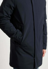 Navyblauwe jas van een gladde stof, met zijzakken en een eenvoudig ontwerp, getoond op taillehoogte.