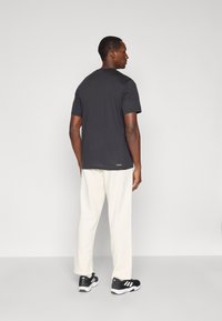 T-shirt preto de manga curta, ajustado, combinado com calças texturizadas de cor creme e sapatilhas atléticas pretas com detalhes brancos.