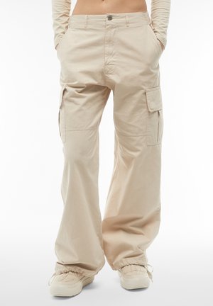 Pantaloni cargo beige con una vestibilità ampia, realizzati in cotone. Presentano tasche laterali, un sistema di chiusura con bottone e polsini elasticizzati alla caviglia.