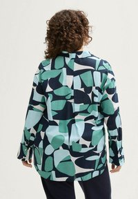 Chemise à manches longues avec un motif abstrait coloré dans des nuances de vert, marine et blanc, avec une coupe décontractée et des poignets à boutons.