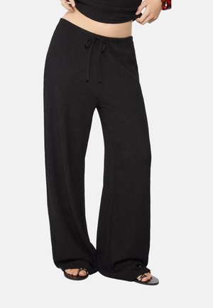 Zwarte wijde broek gemaakt van zachte stof met een gestructureerde afwerking. Heeft een tailleband met trekkoord en licht uitlopende pijpen, met open zoom.