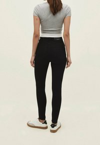 Jeans negros ajustados con cintura alta y bolsillos traseros, combinados con una camiseta corta gris y zapatillas blancas con suelas marrones.