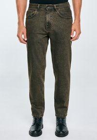 Jeans de mezclilla caqui con corte recto, cinco bolsillos y pasadores para cinturón. Llevados con botas negras de cordones con suela texturizada.