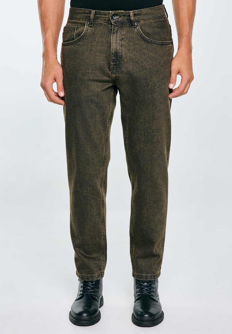 Jeans de mezclilla caqui con corte recto, cinco bolsillos y pasadores para cinturón. Llevados con botas negras de cordones con suela texturizada.