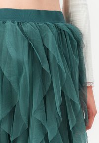Teal tyllskjørt med lagdelt, volangdesign og elastisk midjebånd, som viser en gjennomsiktig, luftig tekstur.