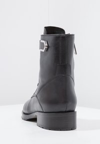 Stivale alla caviglia in pelle nera con tacco spesso, caratterizzato da un dettaglio in metallo con fibbia sulla parte laterale e texture liscia. Cuciture decorative lungo la cucitura posteriore.
