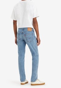 Jeans de mezclilla azul claro con corte recto, bolsillos traseros visibles y un parche de cuero en la cinturilla. Combinados con una camiseta blanca lisa.