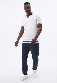 Hvid strikket polo med grønne og marineblå striber ved kraven og kanten. Sammen med marineblå bukser og hvide sneakers.