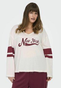Bílé oversized tričko s výstřihem do V, vínovým potiskem "New York U.S.A." a kaštanovými pruhy na rukávech. Má roztrhaný lem.