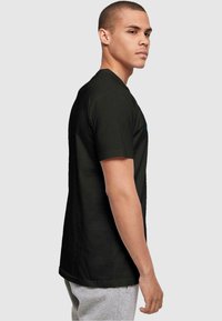 Zwart t-shirt met korte mouwen van katoen, met een ronde halslijn en een subtiele grafische detail op de voorkant. Model in zijprofiel weergegeven.