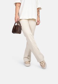 Pantalons longs beige avec des bords effilochés, un haut blanc ample, et un petit sac à main en imprimé léopard marron. Baskets beige et crème.