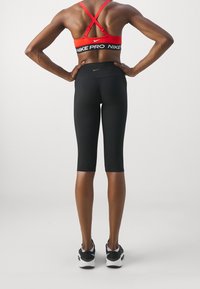 Czarne legginsy Nike Pro z wysokim stanem, zestawione z czerwonym stanikiem sportowym z krzyżowym tyłem i białymi akcentami logo Nike.