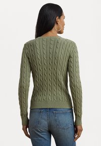 Pull en maille torsadée verte avec des poignets et un ourlet côtelés, mettant en valeur un motif texturé. Assorti à un jean en denim. Vue de l'arrière.