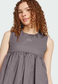 Grå utanärmad klänning med en rynkad midja, tillverkad av lättviktsmaterial, med en subtil logotyp på bröstet. Slät textur och flödig design.