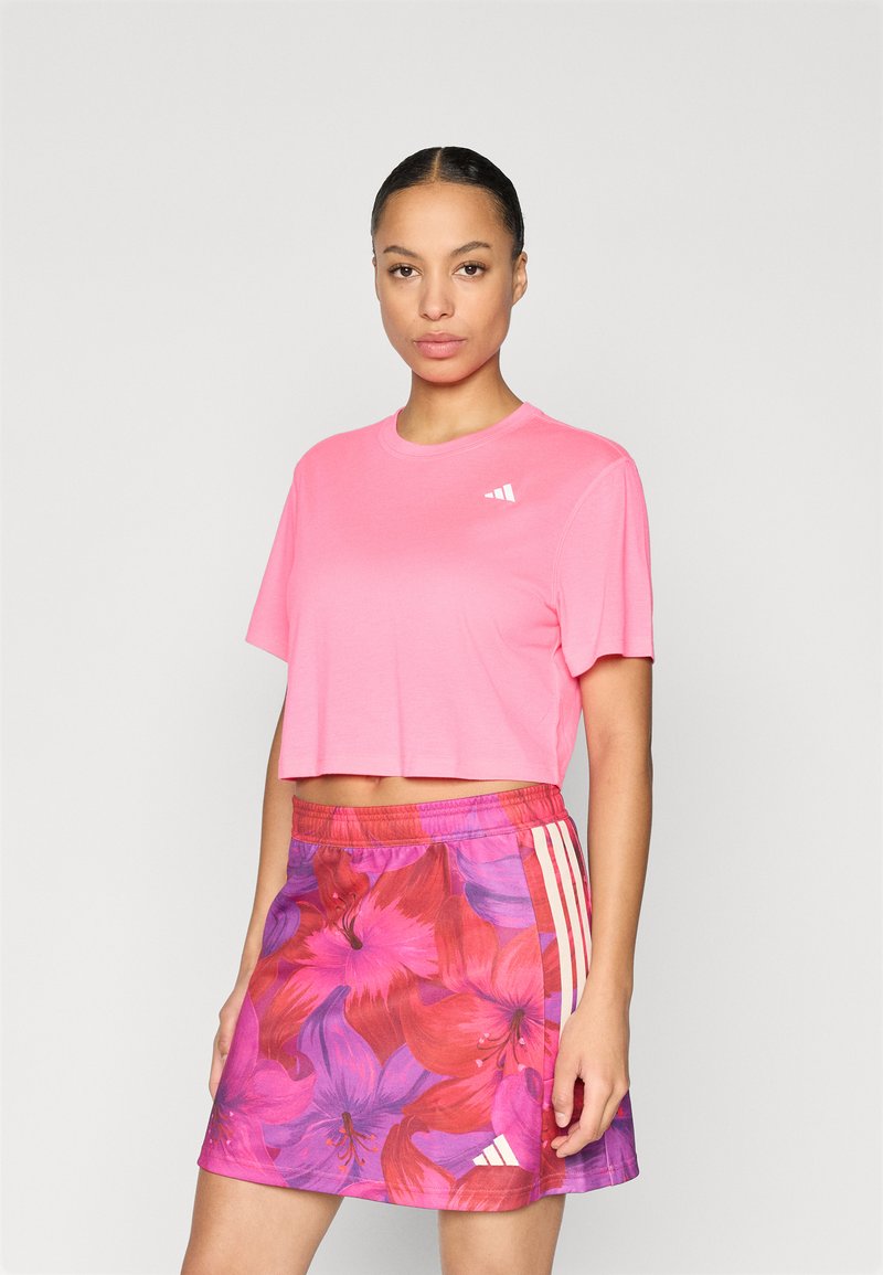 Ροζ κοντομάνικη μπλούζα από μαλακό ύφασμα, συνδυασμένη με μωβ φούστα με λουλουδάτο μοτίβο που περιλαμβάνει κόκκινα και ροζ άνθη και λευκές ρίγες στο πλάι.