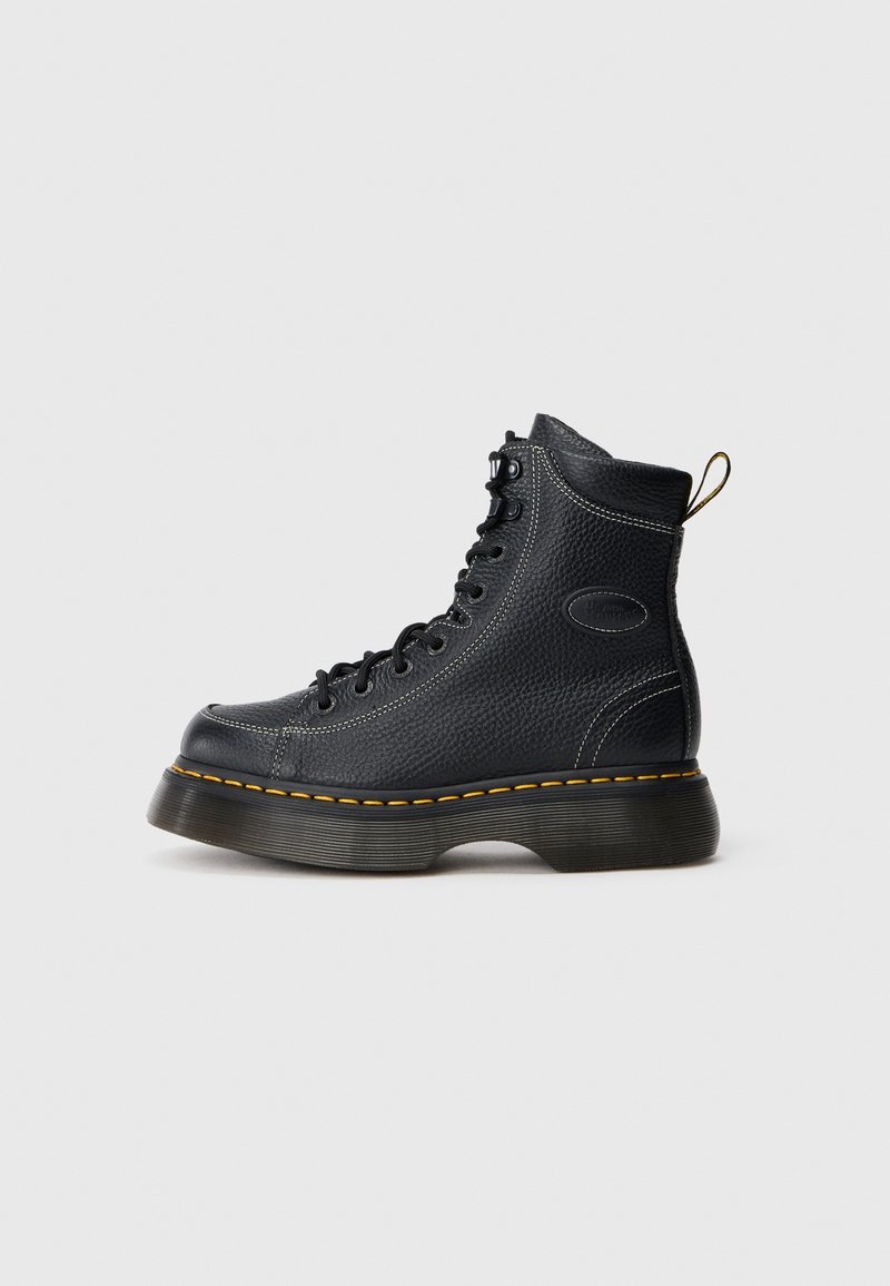 Botte haute en cuir noir avec une semelle épaisse, une couture jaune le long de la semelle, un laçage à l'avant et une languette au talon.