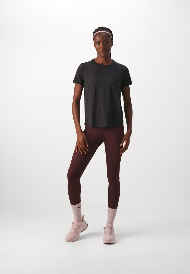 Schwarzes Sport-T-Shirt, kastanienbraune Leggings, rosa Sportschuhe und passende Socken. Zeigt das Nike-Logo auf dem T-Shirt und den Schuhen.