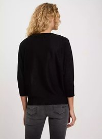 Czarny tylny widok na sweter dzianinowy z rękawami o długości trzech czwartej, z okrągłym dekoltem i lekko strukturalnym wykończeniem. Połączony z ciemnymi dżinsami.