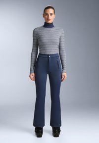 Dopasowana bluzka z długim rękawem w szarym wzorzystym materiale, z golfem. Granatowe rozkloszowane spodnie z przednimi kieszeniami na zamek i gładką fakturą.