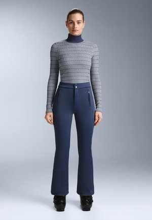 Top s dugim rukavima, krojen u sivoj tkanini s uzorkom, u stilu rolke. Tamnoplave hlače širokih nogavica s prednjim džepovima na patentni zatvarač i glatkom teksturom.