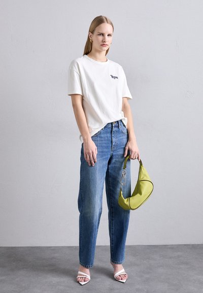 White cotton t-shirt with navy text, blue straight-leg jeans, and a green shoulder bag with silver hardware. White open-toe sandals.