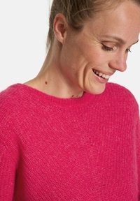 Rosa gestrickter Pullover mit lockerem Schnitt, Rundhalsausschnitt und weicher Textur. Leichter Stoff mit einem dezenten, flauschigen Muster.