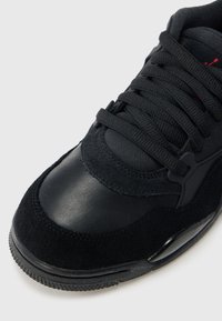 Pantof sportiv negru, realizat dintr-o combinație de piele netedă și materiale din piele întoarsă, cu șireturi texturate și accente subtile roșii pe logo.