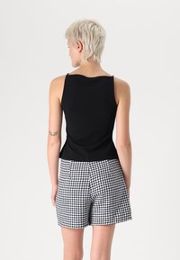 Čierny bezrukávový top s okrúhlym výstrihom, kombinovaný s šortkami s vysokým pásom, ktoré majú čierno-biely vzor houndstooth.