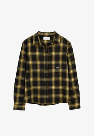Chemise à manches longues à carreaux jaunes et noirs avec col et deux poches poitrine, présentée sur un fond blanc.