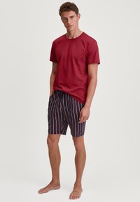 Rode katoenen t-shirt gecombineerd met marineblauwe en meerkleurig gestreepte shorts, met een elastische tailleband, boven de knie lengte, en blote voeten.