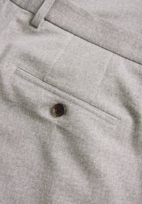 Pantalones de tela gris con una textura fina, que presentan un bolsillo trasero y un botón marrón con un detalle de logo.