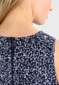 Marinblå ärmlös klänning med intrikata paljettdekorationer i nyanser av blått och silver, med en diskret dragkedja bak.