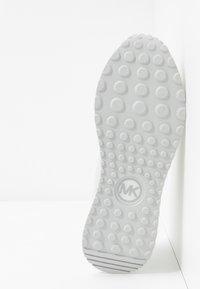 Sole boty s texturovaným, tečkovaným vzorem. Šedý gumový materiál má kruhové prohlubně a logo MK ve středu.