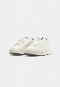 Baskets blanches avec une tige en cuir lisse, bout rond, lacets plats et semelle en caoutchouc texturée. Design minimaliste sans motifs ni accents visibles.