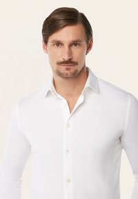 Witte blouse met lange mouwen, gemaakt van een soepele stof, met een knoopsluiting en parelachtige knopen aan de voorkant. Eenvoudig ontwerp.