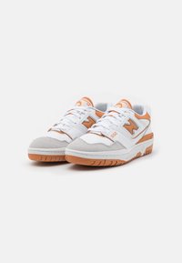 Zapatillas deportivas blancas con acentos naranjas, con una puntera de ante, detalles perforados y una suela de goma texturizada. Número de modelo 550.