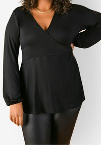 Svart långärmad topp med V-ringning och insvept design, tillverkad av mjukt tyg. Har en avslappnad passform och något utsvängd fåll.