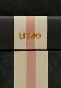 Matériau texturé noir avec un accent rayé beige et rose. Le nom de la marque « LIU JO » est embossé en doré sur la section beige.