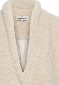 Beige, gestructureerde fleece badjas met een sjaalkraag, V-hals en een label met de tekst "ANDCOWOMAN." Zacht, warm materiaal met een gezellige uitstraling.