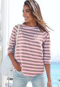 Rosa und braun gestreiftes Langarmoberteil mit weitem Ausschnitt und dem Text "ELB SAND" auf der Brust, kombiniert mit hellblauen Jeans und einer Tasche.