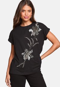 Top negro de manga corta con bordado de flores en lentejuelas plateadas y tonos metálicos, con un corte holgado y escote redondo.