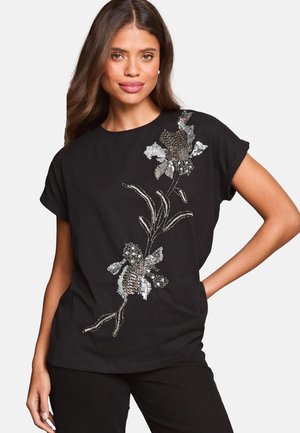 Fekete rövid ujjú felső ezüst és fémes tónusú virágos flitteres hímzéssel, laza szabással és kerek nyakkivágással.