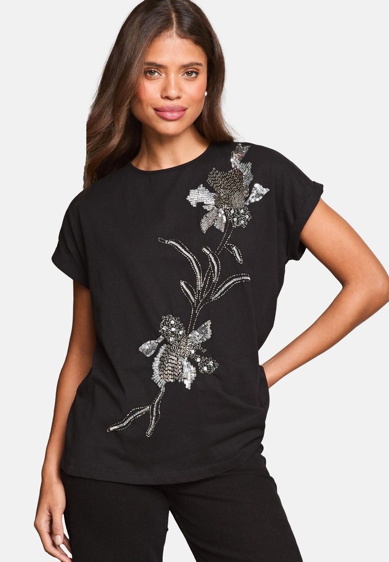 Top negro de manga corta con bordado de flores en lentejuelas plateadas y tonos metálicos, con un corte holgado y escote redondo.