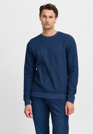 Navy blue sweatshirt with a textured finish, crew neck, and ribbed cuffs. Paired with dark blue jeans.